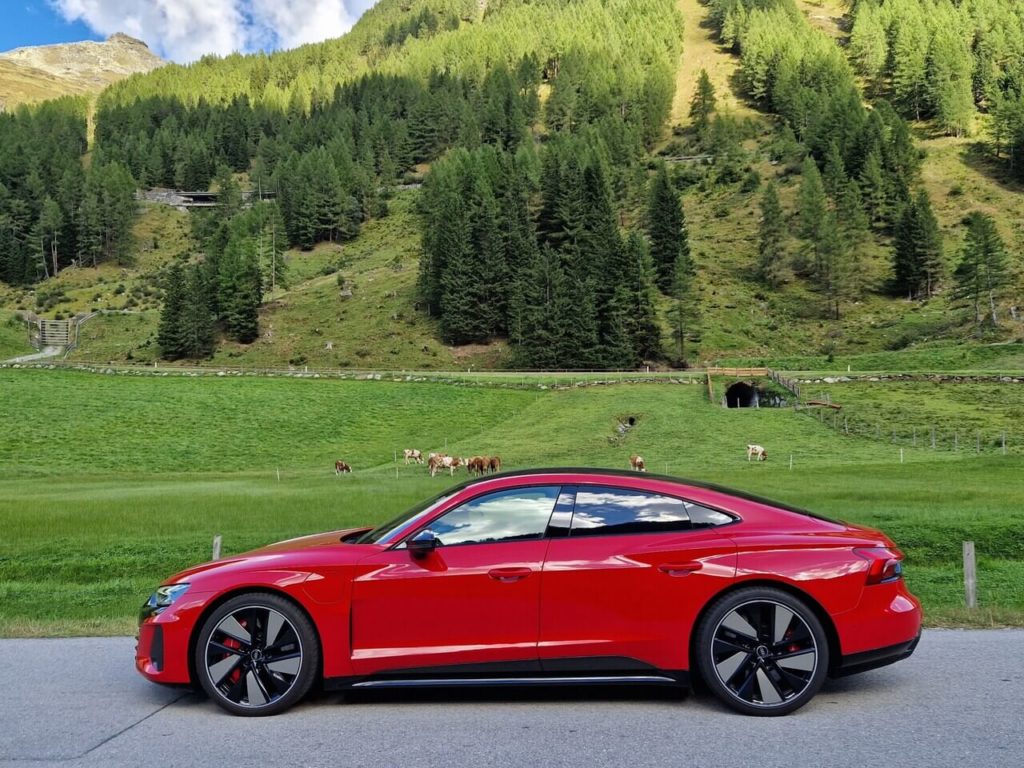Silhouette des Audi RS e-tron GT in Tangorot Metallic mit Kuh-Weide im Hintergrund