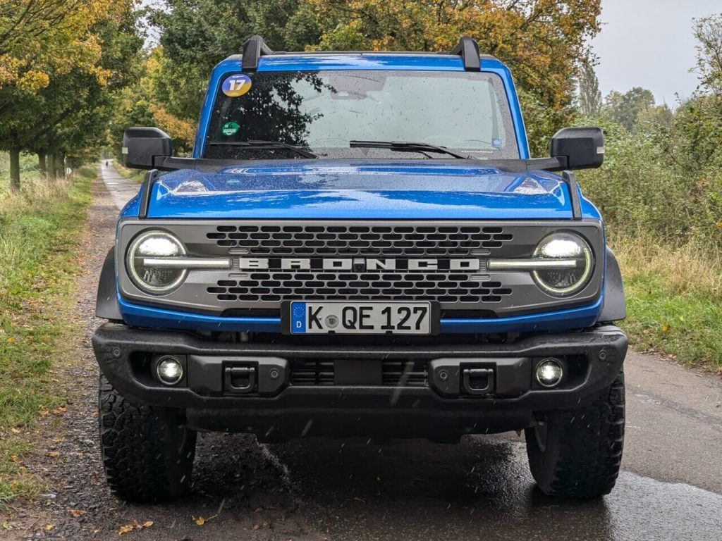 Frontansicht: Ford Bronco Badlands (2025) in der Lackierung Velocity Blue Metallic PN4GL. Grauer Kühlergrill und metall-Stoßfänger mit Befestigungsschlafen für Seile.
