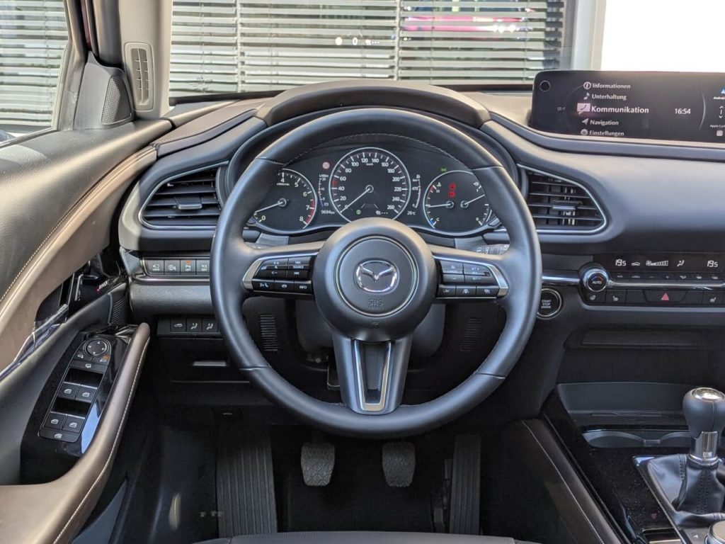 Lenkrad im Mazda CX-30 (2025) - Fahrerperspektive auf analoge Rundinstrumente mit zentralem digitalen Kombiinstrument.