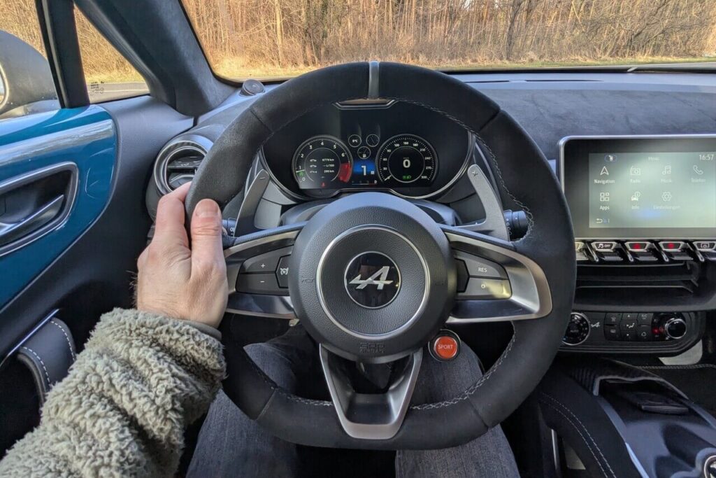 POV: Fahrerperspektive beim Alpine A110 GTS: Alcantara-Sportlenkrad mit grauer 12-Uhr-Markierung und großen Schaltpaddels.