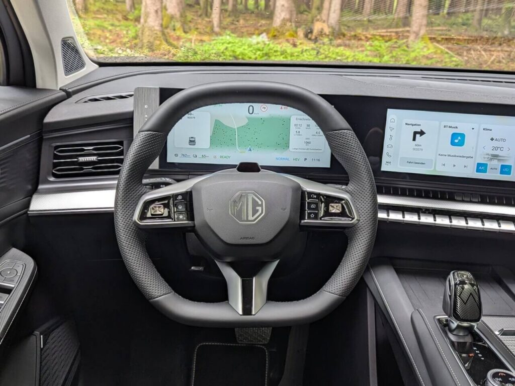Fahrerperspektive beim MGS9 PHEV: 12,3 Zoll Fahrerdisplay, oben und unten abgeflachtes Lenkrad mit perforiertem Kunstleder im Griffbereich.